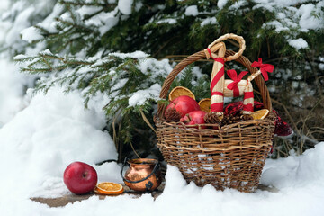 wicker basket with straw Yule Goat toy and apples, witch cauldron in snowy forest. Winter nature...
