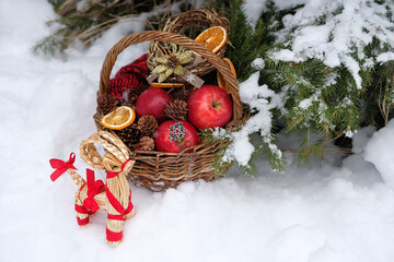 Straw Yule Goat toy and wicker basket with apples, seasonal decorations in snowy forest. Winter...