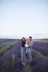 young beautiful happy smiling family: dad, mom and little red-haired daughter, whom dad holds in his arms, stand in lavender field