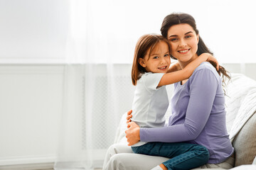 Portrait of happy pregnant woman and her little daughter hugging each other at home