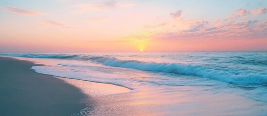 Fototapeta premium Soft pink and blue sunset sky over a calm ocean with waves gently rolling onto a sandy beach.