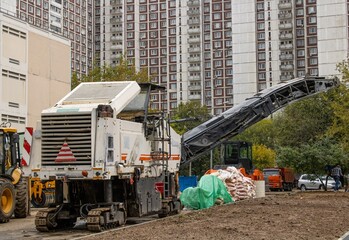 Obraz premium A machine cuts asphalt at a construction site near tall buildings