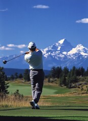 Obraz premium A golfer swings at a beautiful mountain golf course under clear blue skies