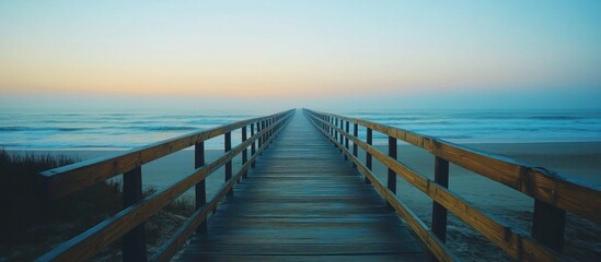 Obraz premium Wooden walkway leading to the ocean at sunrise with a foggy horizon.