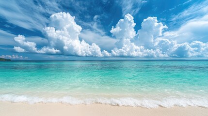 Obraz premium Clear turquoise waters softly caress a pristine sandy beach beneath a bright sky filled with fluffy clouds creating a serene atmosphere