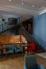 cozy vintage interior of the cafe restaurant with blue walls, wooden floors and brickwork. blue and red chairs are arrenged around tables. natural lighting and lamps.