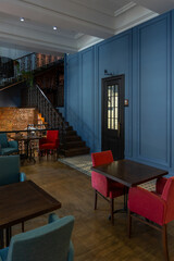cozy vintage interior of the cafe restaurant with blue walls, wooden floors and brickwork. blue and red chairs are arrenged around tables. natural lighting and lamps.