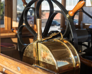 a black steering wheel and a machine telegraph on an old steamer in the captain's cabin