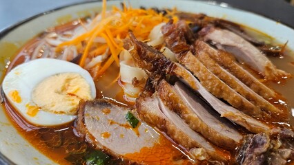 Close-up of a bowl of ramen with pork, egg, and vegetables in rich broth