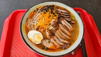 Bowl of ramen with pork, egg, and vegetables on a red tray