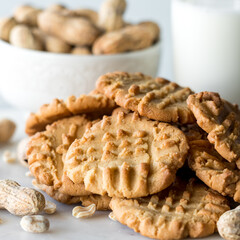A pile of peanut butter cookies, with a bowl of peanuts and a glass of milk.