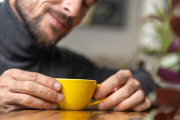 Close-up happy young man smiling in a cafe holding a cup of matcha tea, art with heart shape milk, cappuccino coffee with foam and heart, espresso coffee, decoration with plants, vegan hot drink