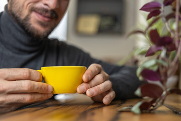 Close-up happy young man smiling in a cafe holding a cup of matcha tea, art with heart shape milk, cappuccino coffee with foam and heart, espresso coffee, decoration with plants, vegan hot drink