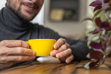 Close-up happy young man smiling in a cafe holding a cup of matcha tea, art with heart shape milk, cappuccino coffee with foam and heart, espresso coffee, decoration with plants, vegan hot drink