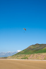 A paraglider flying in the blue sky above Rhossili Bay on the Gower Peninsula, South Wales