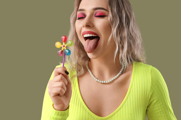 Young woman with lollipop showing tongue on green background, closeup