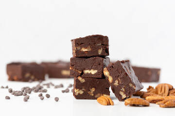 Close Up of Chocolate Pecan Fudge on a White Background with Chocolate Pieces and Pecans Scattered Around