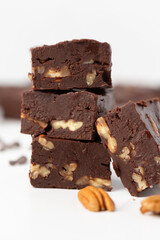 Close Up of Chocolate Pecan Fudge on a White Background with Chocolate Pieces and Pecans Scattered Around