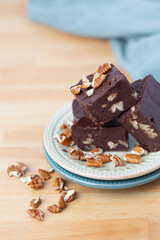 Three Pieces of Homemade Chocolate Pecan Fudge on a Plate with Pecan Pieces Scattered Around on a Kitchen Countertop