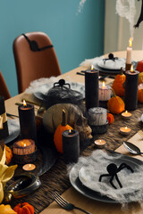 Festive table setting for Halloween party with burning candles, pumpkins, spiders and web