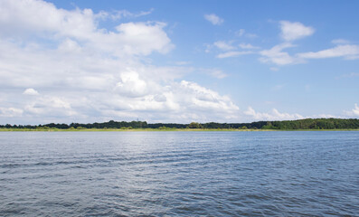 Serene landscape of a calm river surrounded by lush greenery under a beautiful blue sky with fluffy clouds, perfect for nature lovers and outdoor enthusiasts.