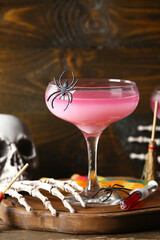 Glass of delicious pink cocktail and skeleton hand for Halloween celebration on wooden background, closeup