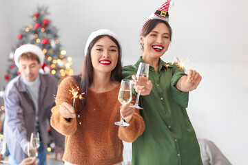 Female friends with champagne and sparklers celebrating New Year at home party