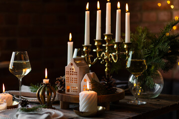 Beautiful table setting for family Christmas dinner at home. Cozy atmosphere, candlelight. Wine glasses, vintage chandelier, elegant interior. Fir tree branches, wooden furniture, dark, bokeh