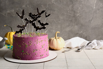 Tasty cake decorated for Halloween on table near grey wall