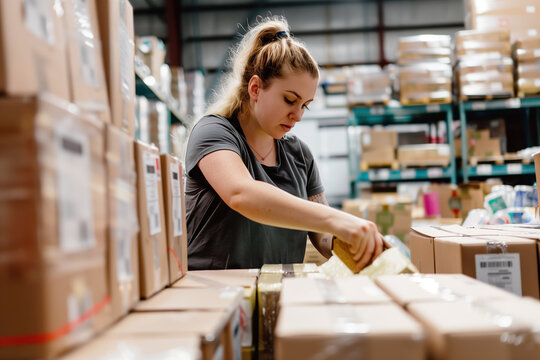 Focused warehouse employee carefully packing products into boxes for shipment in a busy storage facility, ensuring efficient order fulfillment and inventory management