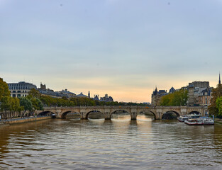 Fototapeta premium Seine River in Paris with stone bridge spanning the water, lined with historic buildings and trees, boats moored along the quay, overcast sky, calm water
