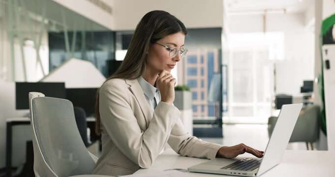 Pensive business woman using laptop in modern office, preparing, editing document, on-line presentation, analyzing received data, working on financial report, researching market trends and information