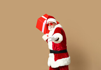 Santa Claus in sunglasses with gift box on brown background