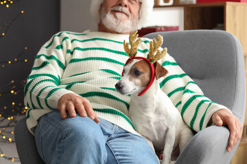 Mature man and cute dog with reindeer horns at home on Christmas eve, closeup