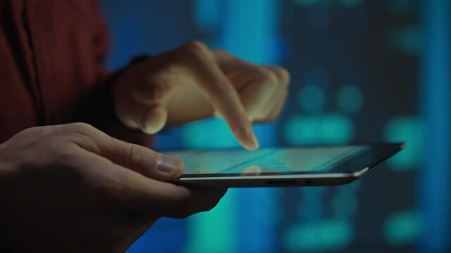 A close-up of a person's hand using a tablet in a data center with blue lights in the background