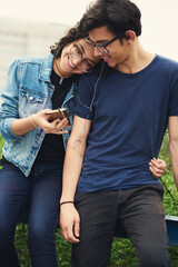 Couple, teenager and music outdoor for relax, bonding and social media together on weekend with romance. Boy, girl and happy for relationship, earphones and listening in park with love connection