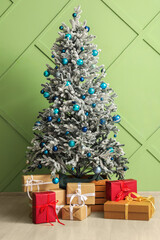 Beautiful Christmas tree and gifts near green wall