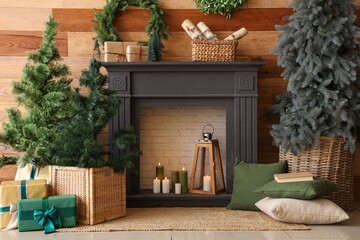 Fireplace with small Christmas trees, gift boxes and wreath near wooden wall