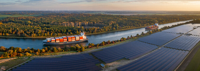 Panorama view of  two large container ships sailing along canal, bordered by vast solar field and...