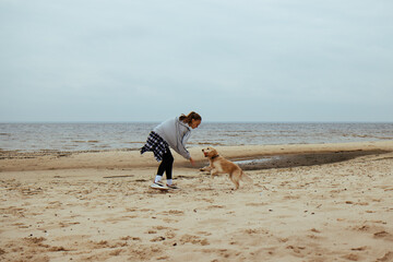 Young woman tossing a ball for her dog by the ocean. The dog races across the sand, bringing back the ball, creating a dynamic and playful beach scene.