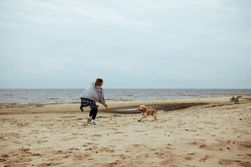 Girl and dog playing by the seaside. The dog happily returns with the ball, capturing the playful bond between them in a serene autumn beach setting.