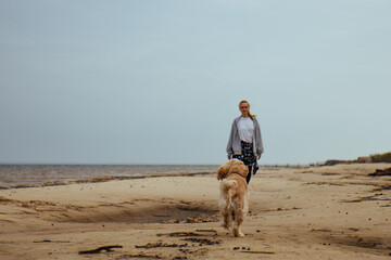 Young woman and her dog playing fetch on the sandy shore. The dog chases after the ball, and the beach setting adds to the dynamic and fun atmosphere.