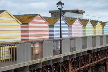 Colorful beach huts lining a pier in a coastal town on a cloudy day showcasing vibrant stripes and unique designs