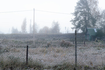 An autumn field with fading grass, bordered by a wire fence and power line poles, lightly shrouded...