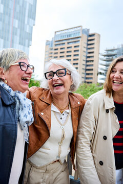 Vertical. Three cheerful only mature Caucasian friends women enjoying walking happy together in urban. Older gray hair tourists female people strolling laughing European sightseeing holidays outdoors 