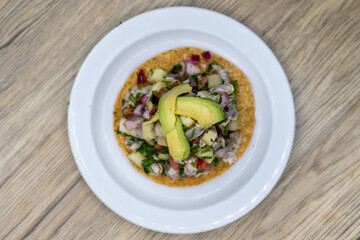 Overhead view of delicious looking shrimp tostada stacked high on a tortilla and topped with sliced avocado for an excellent Mexcian seafood meal