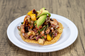 Delicious looking tostada exotica stacked high on a tortilla and topped with chopped fruit and avocado for an excellent Mexcian seafood meal