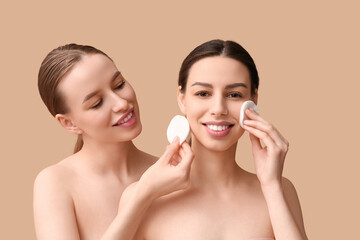Beautiful young happy women with healthy skin and cotton pads on beige background