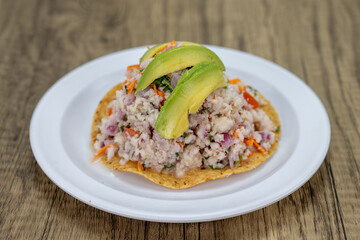 Delicious looking fish tostada stacked high on a tortilla and topped with sliced avocado for an excellent Mexcian seafood meal