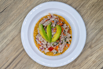 Overhead view of delicious looking fish tostada stacked high on a tortilla and topped with sliced avocado for an excellent Mexcian seafood meal